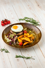 Juicy steak with cheddar cheese, fried potatoes, cherry tomatoes and baked egg served on white wooden background in rustic style with copy space