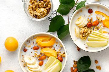Granola bowl with fruits, nuts, milk and peanut butter in bowl on a white background. Healthy breakfast cereal top view