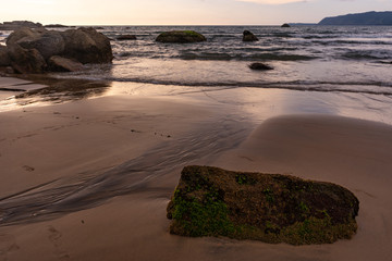 mossy green rocks at the beach of agonda at sunset in goa, india