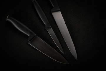 Minimalism on a black background. Abstract of three kitchen knives close up. Beautiful metal texture. Banner or for design.