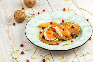 potato pancakes with salmon, cranberries and tartar sauce on white wooden background, lunch menu of food restaurant in rustic style