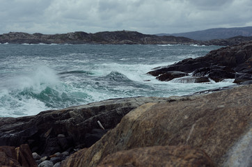 Severe gloomy norway landscape with stormy sea - grey waves of Arctic Ocean in gale and black granite rocks in cloudy weather, surf.