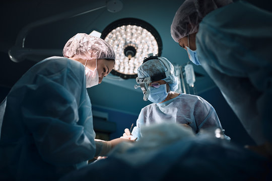Medical team in the operating room, dark background. The theater of the operating room, an international team of professional doctors in a modern operating room are conducting an operation. Saving - Powered by Adobe