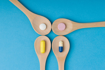 Wooden spoons full of pills, tablets, drugs, gel capsules .  Blue background.