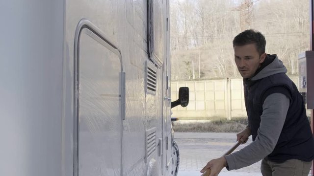 A young man of European nationality washes a car at a car wash. Self catering. Seasonal RV Recreational Vehicle Motorhome Cleaning Using Pressure Washer. RV Camper. Caucasian Men