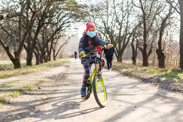 Fototapeta premium Little girl wearing medical mask prevent flu, pollutions and covid-19 riding bicycle outdoor.
