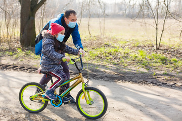 Caucasian father helping daughter ride bicycle wearing protection mask for protect pm2.5 and Coronavirus Covid-19 Pandemic virus symptoms.