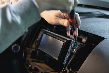 Auto technician is installing a new car radio player close up.