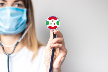 female doctor holding a stethoscope on a light background. Added flag of Burundi. Concept medicine, level of medicine, virus, epidemic
