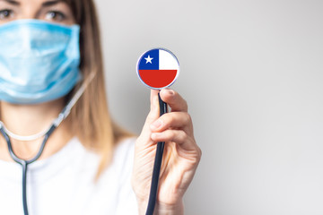 female doctor in a medical mask holds a stethoscope on a light background. Added flag of Chile....