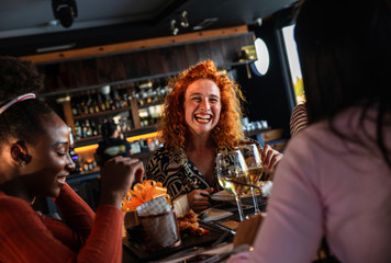 Group of young female friends having fun in restaurant, talking and laughing while dining at table.