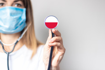 female doctor in a medical mask holds a stethoscope on a light background. Added flag of Poland. Concept medicine, level of medicine, virus, epidemic