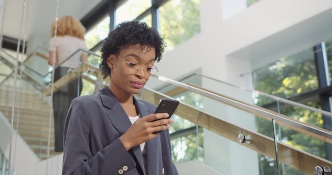 Young woman office manager using smartphone with different face expressions. Successful businesswoman looking at her mobile phone screen while standing at office . People, work, tech. Indoors.