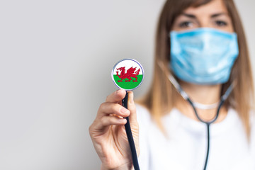 female doctor in a medical mask holds a stethoscope on a light background. Added flag of Wales....