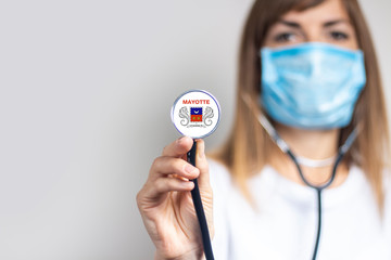 female doctor in a medical mask holds a stethoscope on a light background. Added flag of Mayotte. Concept medicine, level of medicine, virus, epidemic