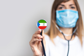 female doctor in a medical mask holds a stethoscope on a light background. Added flag of Equatorial Guinea. Concept medicine, level of medicine, virus, epidemic