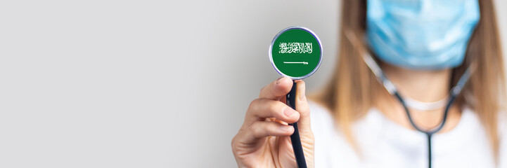 female doctor in a medical mask holds a stethoscope on a light background. Added flag of Saudi...