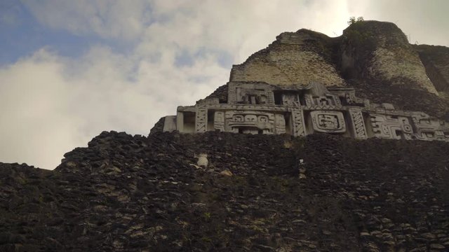 Slide right looking upward at Xunantunich Mayan carvings on the pyramid in Belize, old ancient ruins, cinematic tilt up introduction to historical site.