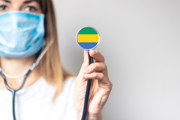 female doctor holding a stethoscope on a light background. Added flag of Gabon. Concept medicine, level of medicine, virus, epidemic
