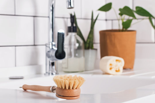 Natural material brush for washing dishes lying near the sink on modern white kitchen.