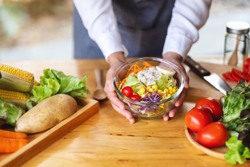 Closeup image of a female chef cooking and holding a bowl of fresh mixed vegetables salad in kitchen