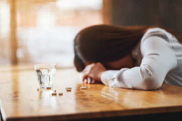 Closeup image of a sick woman sleep on table with white pills and a glass of water