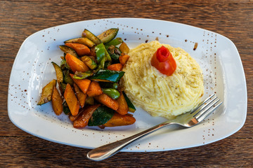 Mashed potatoes with fried vegetables on a white plate.
