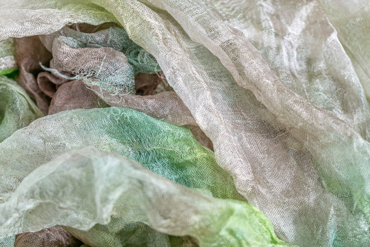 Large folds of sparse Margilan silk of green, brown and white color, background texture of textiles.