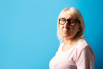 Old woman in glasses on a blue isolated background. The concept of sarness, care for old people, good eyesight. Banner. copy space