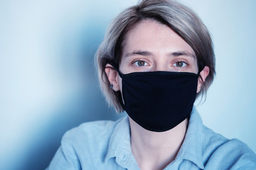 Portrait of a sad woman in a black mask on a white wall in isolation during a pandemic - virus corona covid 19