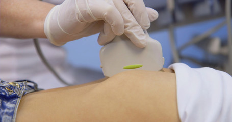 Doctor is making abdominal ultrasound for child girl using scanner machine in clinic, side view. Woman runs ultrasound sensor over patient tummy in clinic. Diagnostic examination of internal organs.