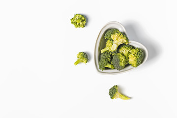 Raw broccoli in a heart shaped bowl on white background,