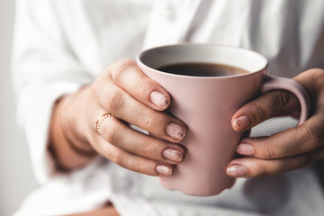 Woman in a white t-shirt holds morning coffee in a pink ceramic cup. Manicure. Front view