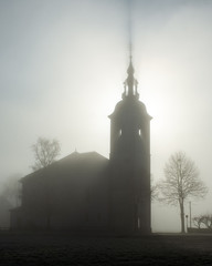 Fototapeta premium Slovenian church surrounded by fog during winter with the sun shining through