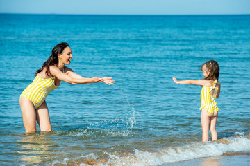 Happy mother with a smiling child 3 years old at the seaside on a splash water in the sea.