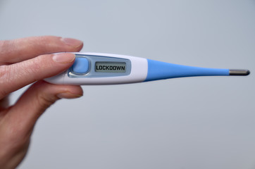 Male hand holds clinical thermometer with lockdown text on the screen during global covid-19 or corona pandemic.