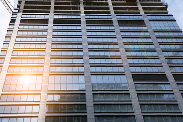 Building under construction and cranes under a cloudy sky. Modern architecture with sun ray.
