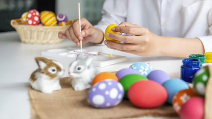 Happy Asian woman painting eggs for Eastertime at home. Family preparing for Easter.