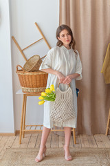 Attractive young girl with long brunette hair hold eco bag with yellow tulips. Zero wasty. Stop polution be resonsible