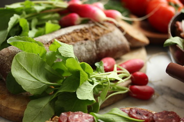 Radish with tops on a wooden board. Bread, tomatoes, sausage on the table. Rustic. Background image, copy space