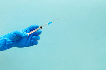 Hand in blue gloves holding syringe isolated on blue background.