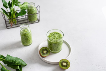 Freshly blended green fruit smoothie in a glass on light background with ingredients. Copy space,...