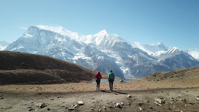 Couple trekking to Ice lake, part of the Annapurna Circuit Trek, Himalayas, Nepal. They are happy. Annapurna chain in the back, covered with snow. Clear weather, dry grass, snowy peaks. High altitude