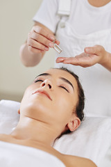 Obraz na płótnie Canvas Beautician applying massage oil on face of young spa salon client