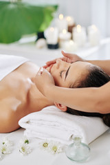 Fototapeta na wymiar Young woman enjoying rejuvenating face massage in beauty salon