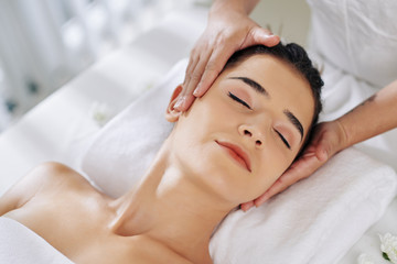 Smiling young woman lying on back and getting face lifting massage
