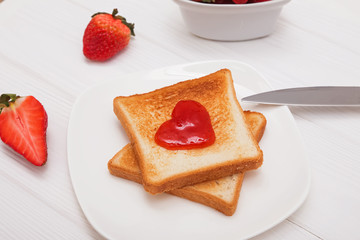 Toasted bread with jam in heart shape and strawberries on the white table.