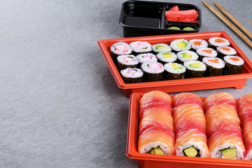Sushi maki with salmon, shrimp and avocado, sushi philadelphia, soy sauce and ginger in a take away plastic container.
