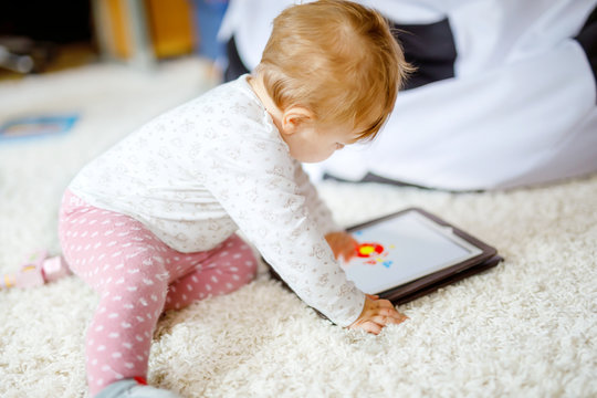 Cute adorable baby girl watching cartoons on tablet pc. Todder child at home touching on screen and playing educational games on computer.