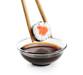 Sushi maki in chopsticks and bowl with soy sauce isolated on white background.